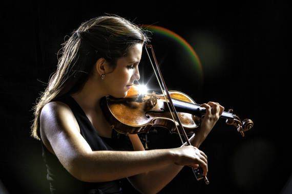 Young woman playing violing during night presentation or concert. Classical Musician.